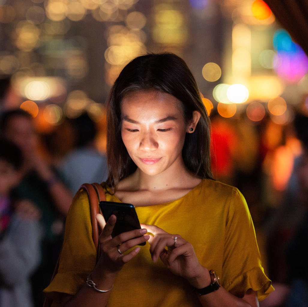 A woman on the street at night, checking messages on her phone.