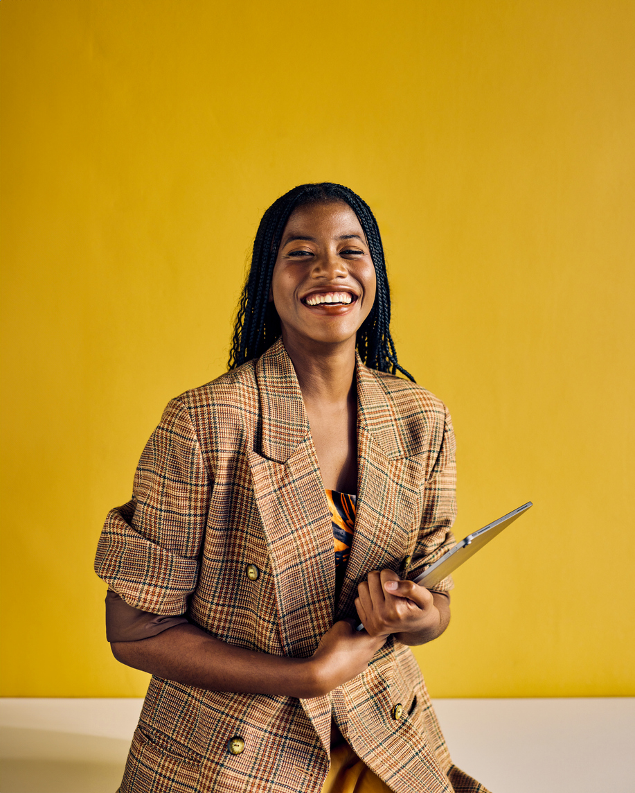 Smiling African American businesswoman in a plaid blazer holding a tablet in a modern office.
