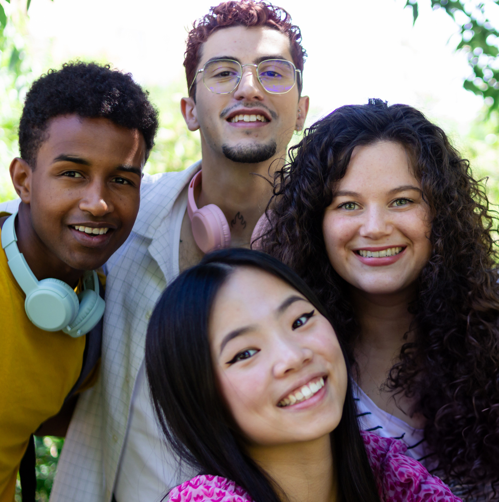 Four cheerful young adults are standing together outside on a sunny day
